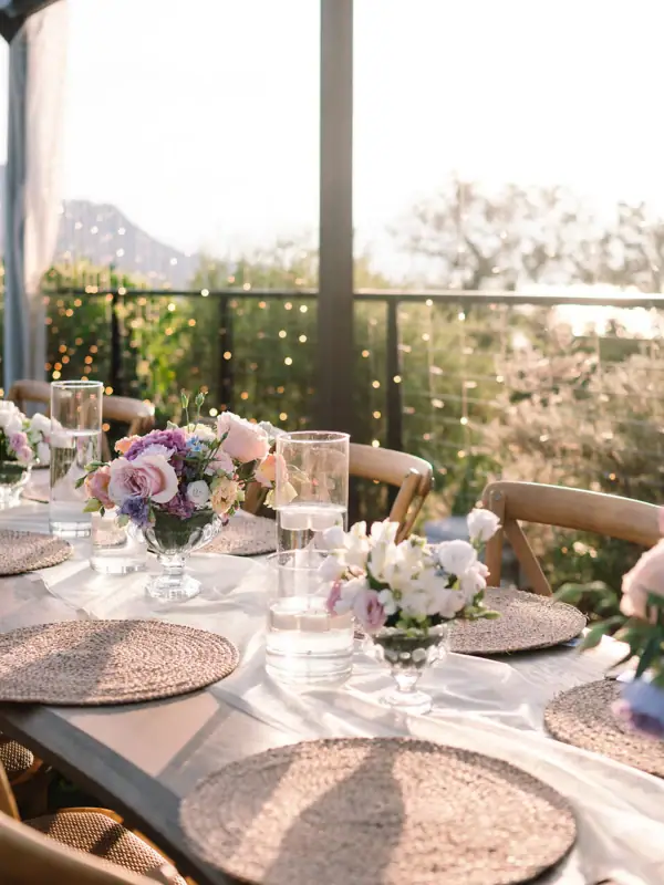 Hochzeitstafel mit Blumenarrangements Festlich gedeckter Tisch im Freien mit weißen Tellern, geflochtenen Platzsets und zarten Blumenarrangements.