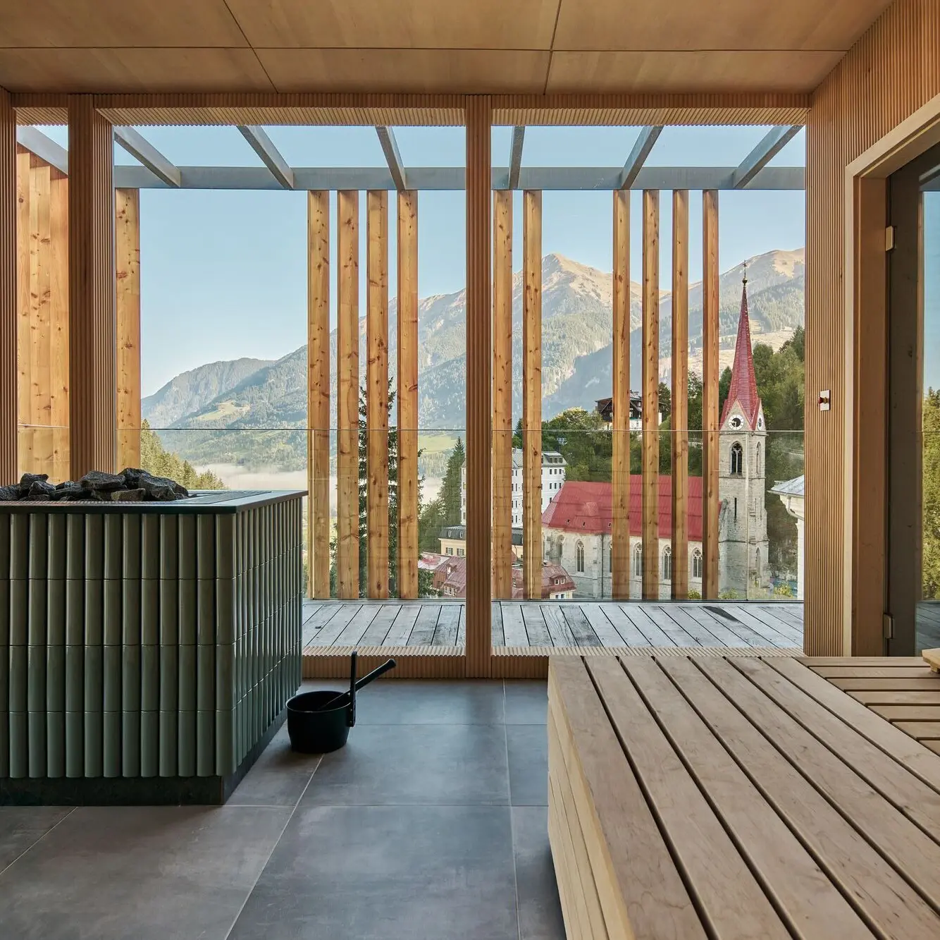 Sauna mit Ausblick Blick aus der Sauna auf das Tal. Im Vordergrund Sitzbänke, dann der Saunaofen und die holzverkleidete Fassade