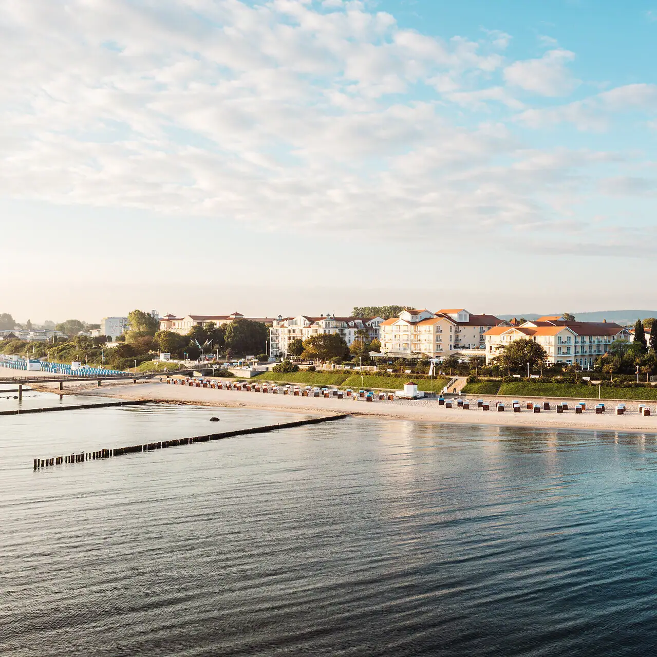 Die Ostsee mit dem Strand und Gebäuden im Hintergrund. Das Ostseehotel Kühlungsborn im Blick.