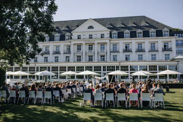 Hochzeit A-ROSA Travemünde Eine Hochzeitsgesellschaft sitzt auf Stühlen bei einer freien Trauung vor dem A-ROSA Travemünde.