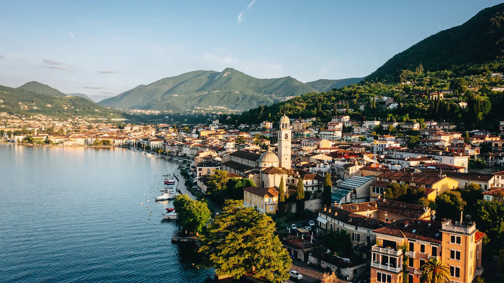 Stadt am Ufer eines Sees mit Bergen im Hintergrund.