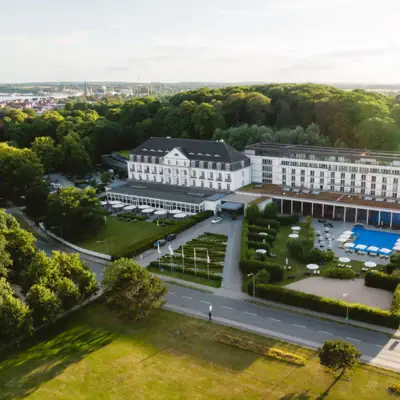 A-ROSA Travemünde Großes weißes Gebäude mit Pool und Bäumen im Vordergrund.