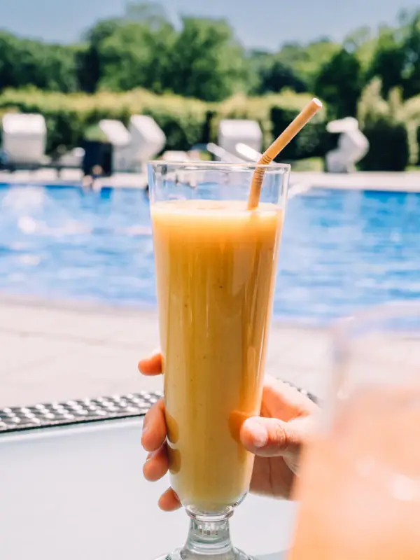 SPA-ROSA Travemünde Eine Person hält ein Glas Orangensaft vor einem Außenpool im Hintergrund..