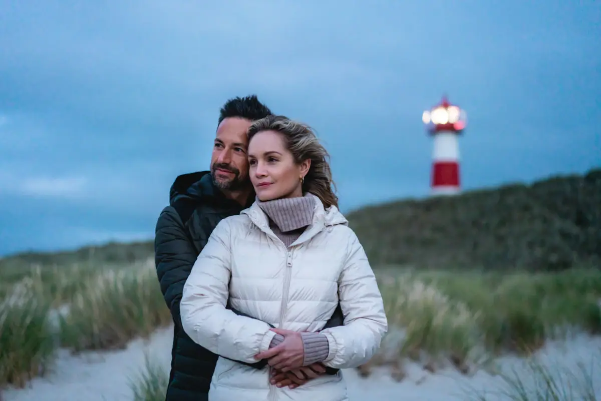 Sylter Dünen Ein Mann und eine Frau stehen am Strand mit einem Leuchtturm im Hintergrund.