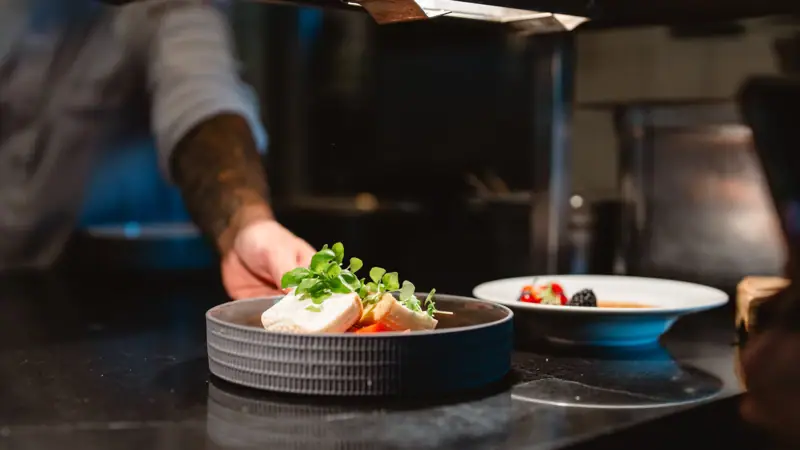 Tellerwerk im A-ROSA Travemünde Eine Person hält Essen in einer Pfanne.