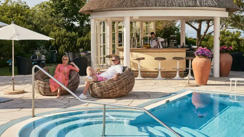 Ein Mann und eine Frau sitzen in Korbstühlen neben einem Pool.