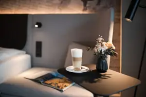 Zimmer Ein Tisch mit einem Getränk und einer Vase mit Blumen darauf.