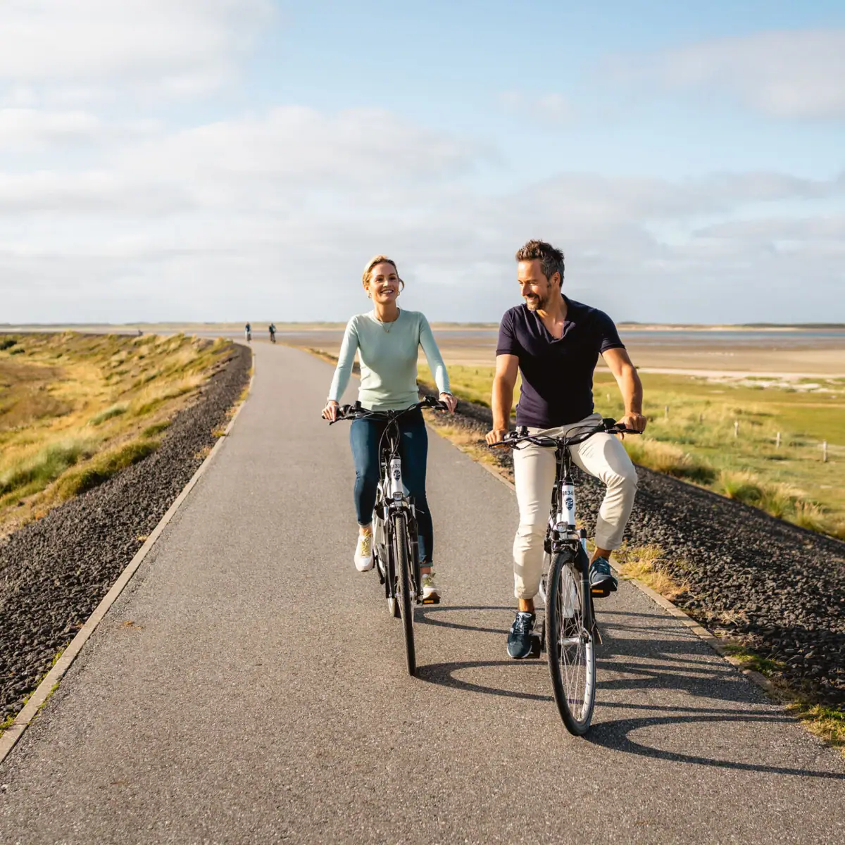 Fahrradtour am Deich Ein Mann und eine Frau fahren auf einer Straße Fahrrad.