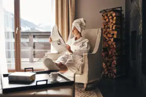 Zimmer Eine Frau im weißen Bademantel liest eine Zeitung in einem Stuhl.