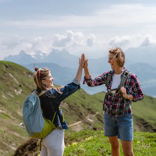Wandern Highfive Zwei Frauen geben sich im Freien ein High Five und Berge sind im Hintergrund zu sehen..