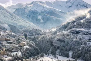 Natur im Winter Verschneiter Berg mit Gebäuden und Bäumen.