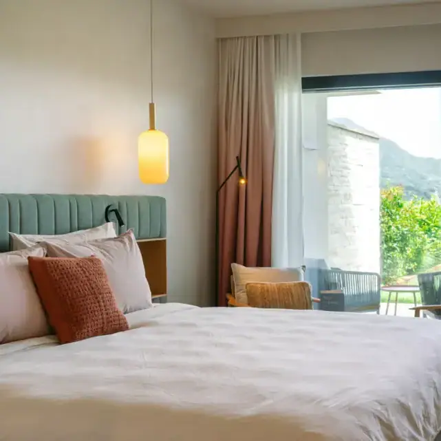 A-ROSA Gardasee Zimmer Hotelzimmer mit Bett, Stühlen und großer Schiebetür zum Garten.