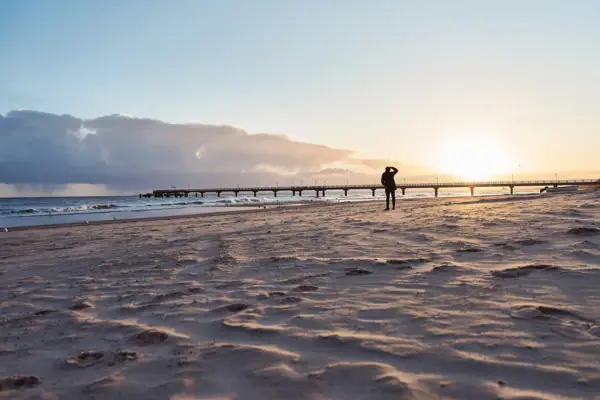 Eine Person spaziert am Strand entlang bei Sonnenuntergang.