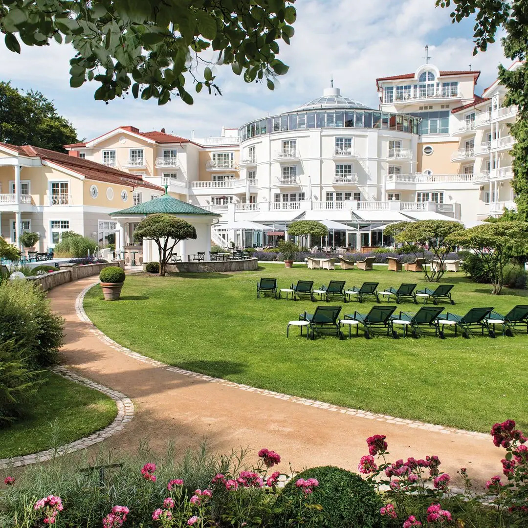 A-ROSA Heringsdorf Außengarten Liegestuhl im Garten mit Bäumen und klarem Himmel im Hintergrund.