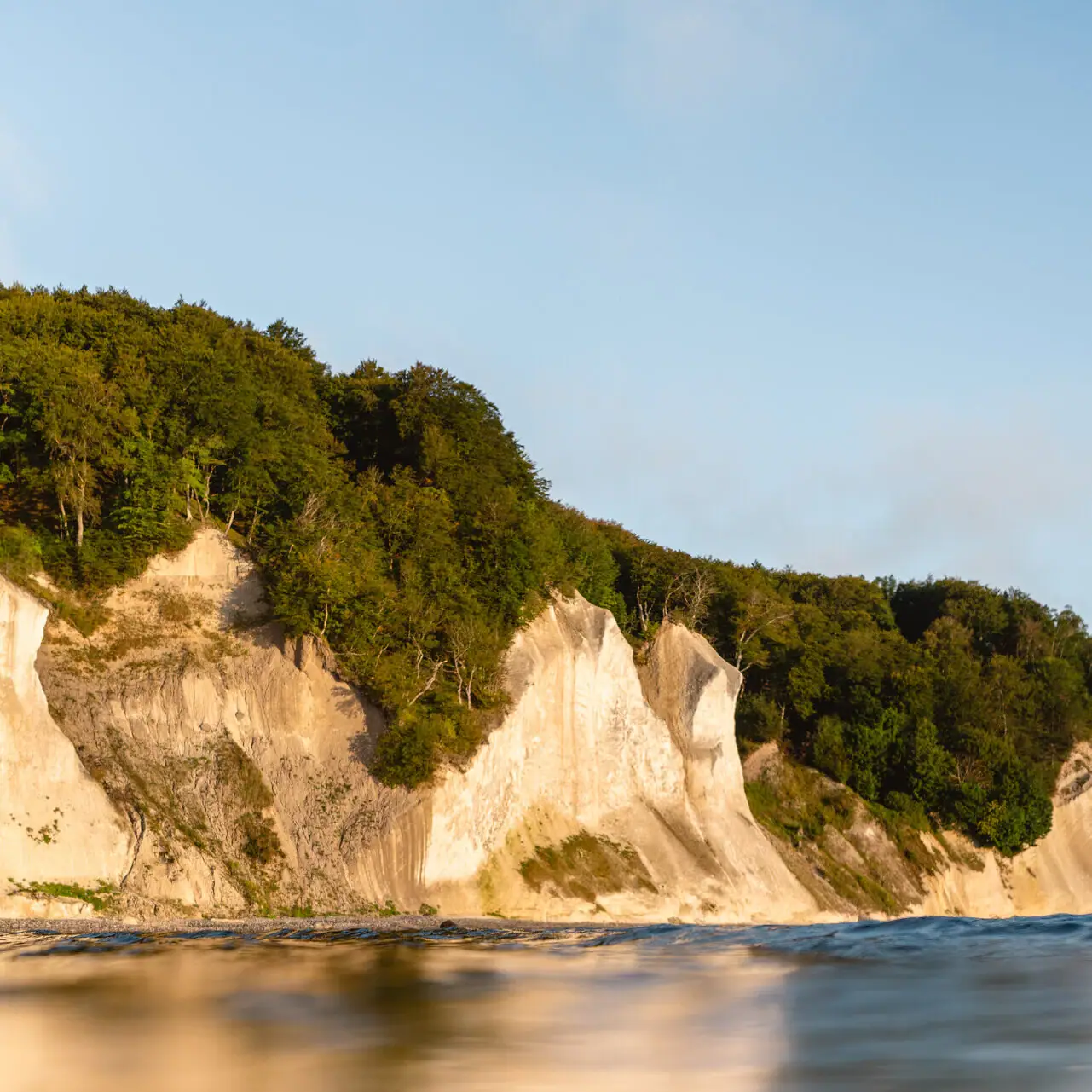 Körper aus Wasser mit Klippe und Bäumen im Vordergrund.