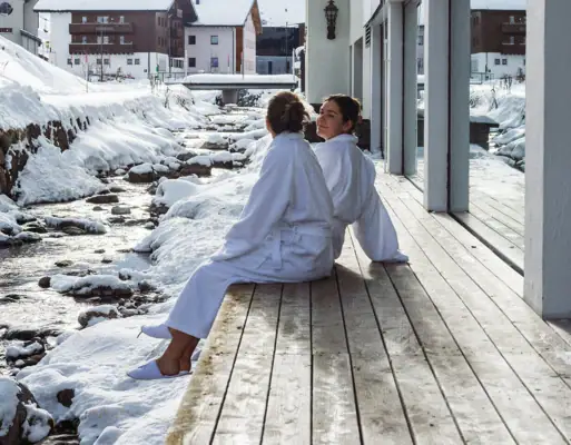 Zwei Frauen sitzen auf einer Veranda vor einem Gebäude im Freien.