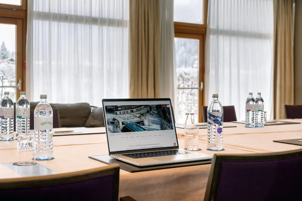 Tagungsraum A-ROSA Kleinwalsertal Ein Laptop steht auf einem Tisch in einem Tagungsraum mit Wasserflaschen und einem Fenster im Hintergrund.