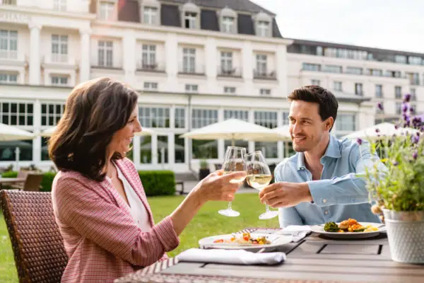 Ein Mann und eine Frau stoßen mit Weingläsern an einem Tisch im Freien an.