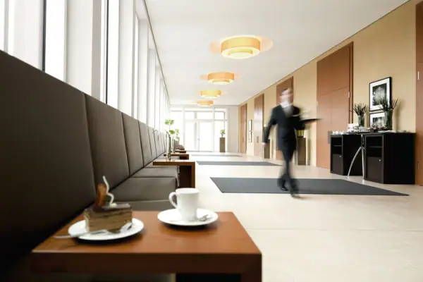 Foyer Ein Mann geht in einem Flur und im Vordergrund ist ein kleiner Tisch mit einem Stück Kuchen und einer Tasse zu sehen.