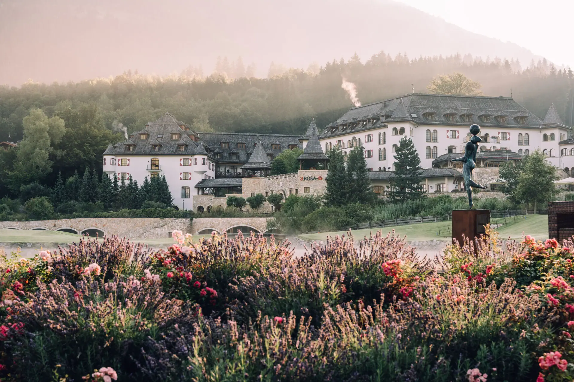 Schlosshotel Kitzbühel Großes Gebäude mit einer Statue im Vordergrund.
