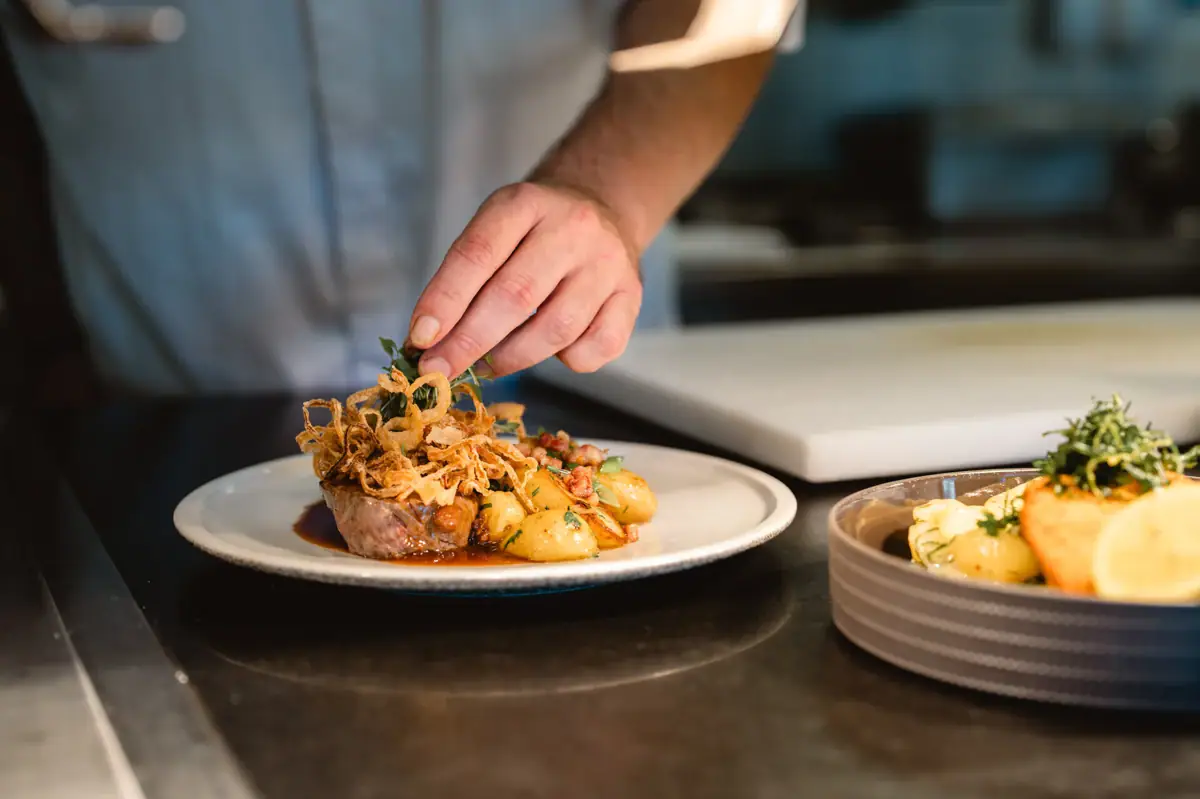 Tellerwerk Eine Person legt Zwiebeln auf ein Gericht.