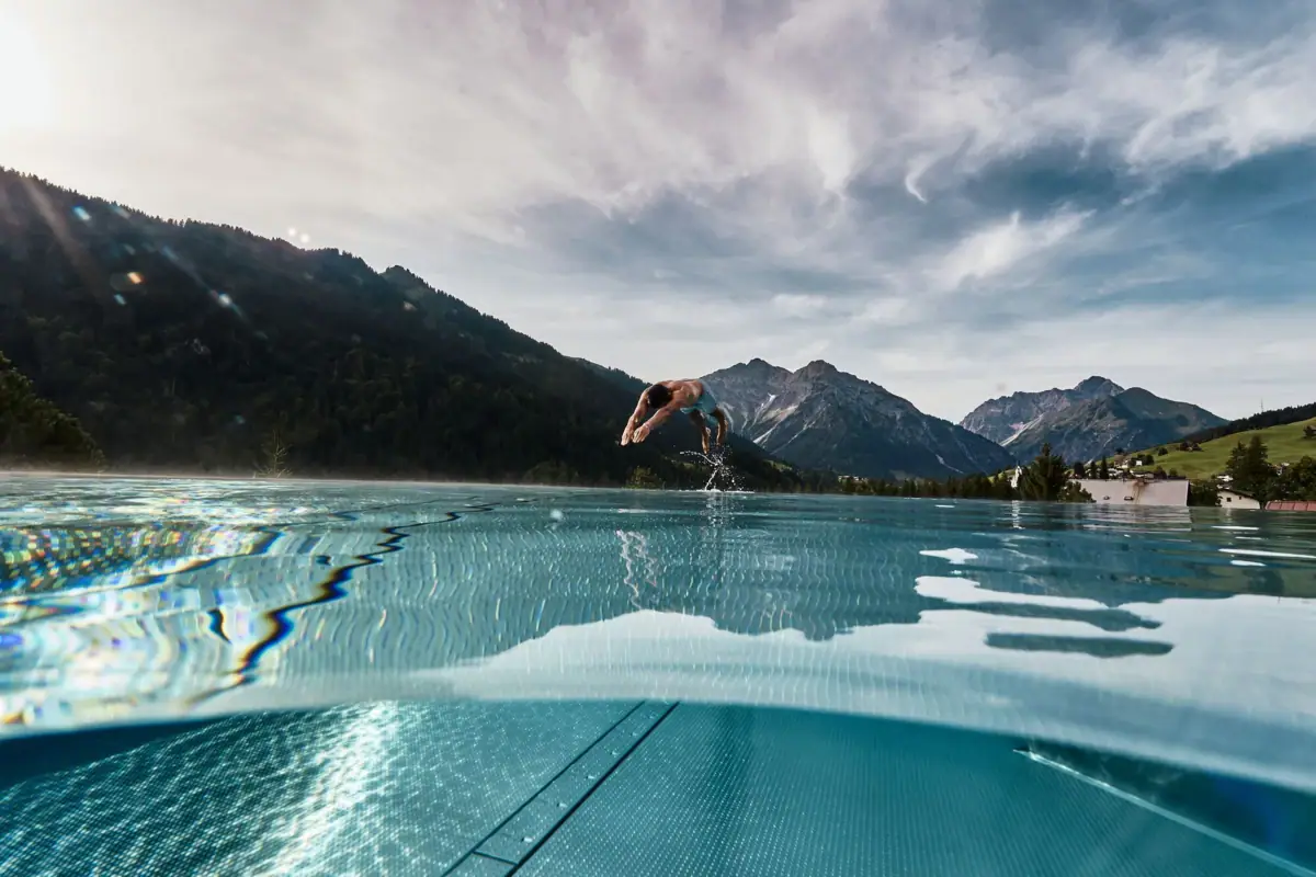 Eine Person springt in einen Pool mit Bergen im Hintergrund.