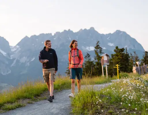 Ein Mann und eine Frau gehen auf einem Weg mit Bergen im Hintergrund.