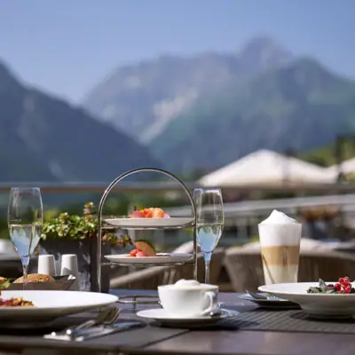 Restaurant Theo's Tisch im Freien mit Geschirr, darunter Teller mit Essen und Getränken mit Bergen im Hintergrund.
