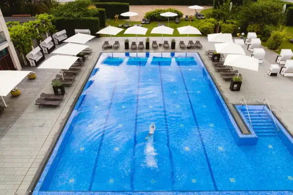 SPA-ROSA Travemünde Eine Person taucht durch ein großes Außenbecken mit einigen Sonnenliegen und Schirmen drum herum.