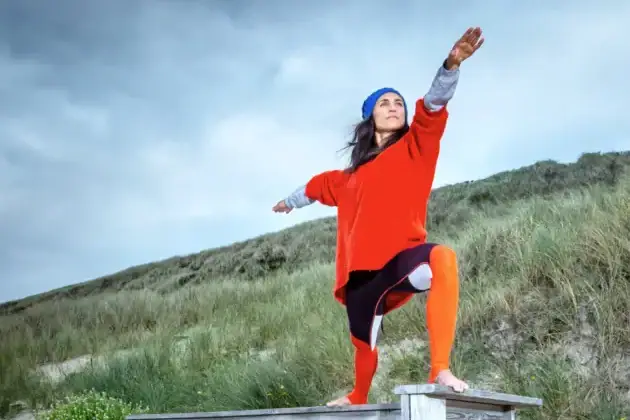 Yoga vor Dünenlandschaft Eine Frau steht mit ausgestreckten Armen auf einer Bank im Freien.