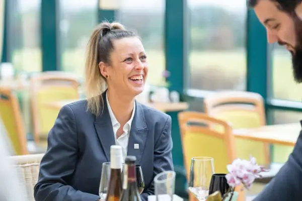 Frau lächelnd an einem Tisch mit Weingläsern.