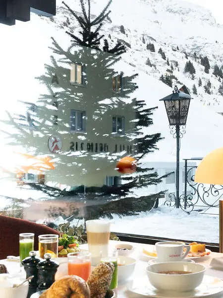 Ein Tisch mit Geschirr und Speisen vor einem Fenster mit schneebedecktem Berg im Hintergrund.