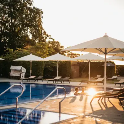 Wellness Ein Außenpool mit Sonnenschirmen und Liegestühlen.