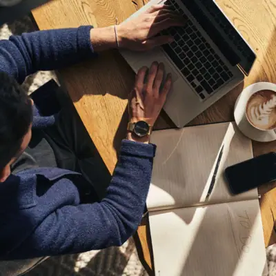 Firmen Kurhaus Binz Person, die einen Laptop auf einem Tisch benutzt, daneben steht eine Tasse Cappuccino.