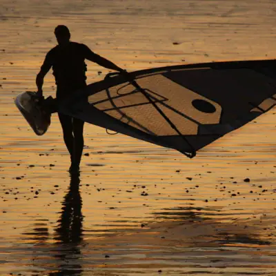 Ein Mann hält ein Segel am Strand.