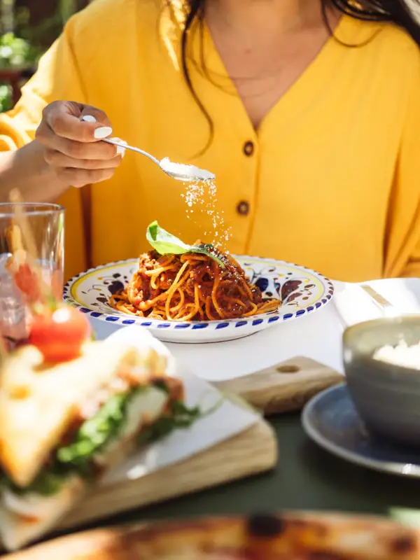 Eine Person streut Salz auf einen Teller Spaghetti.