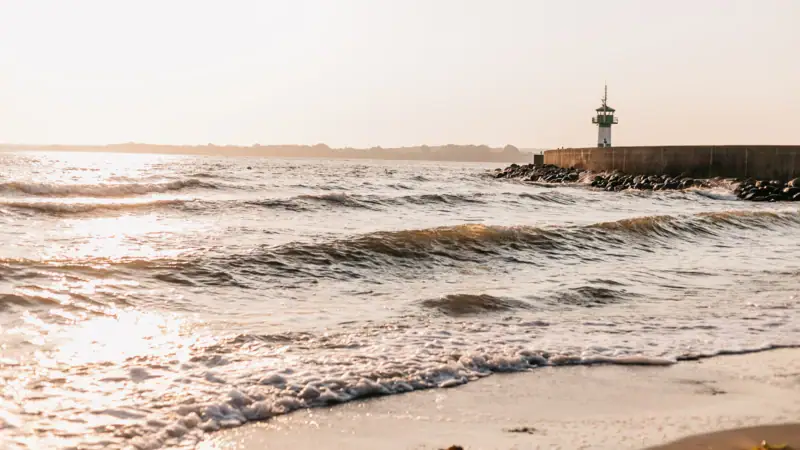 Ein Gewässer mit einem Leuchtturm am Ufer.