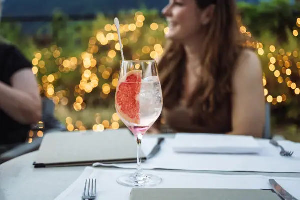 Trattoria im A-ROSA Gardasee Ein Drink mit einer Scheibe Grapefruit auf einem Tisch im Freien.