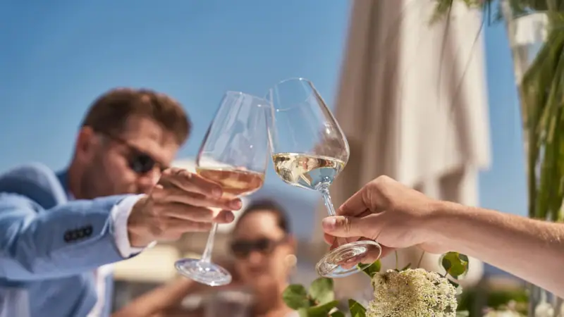 Private Feier auf Rügen Eine Gruppe von Menschen stößt im Freien mit Weingläsern an und im Hintergrund ist der blaue Himmel zu sehen.