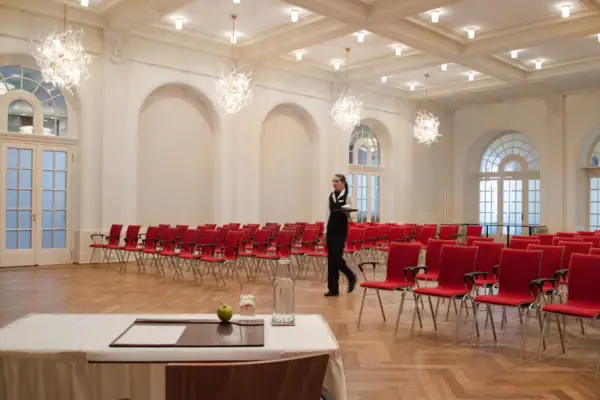Tagungsraum Travemünde Eine Frau geht in einem großen Tagungsraum mit vielen roten Stühlen.