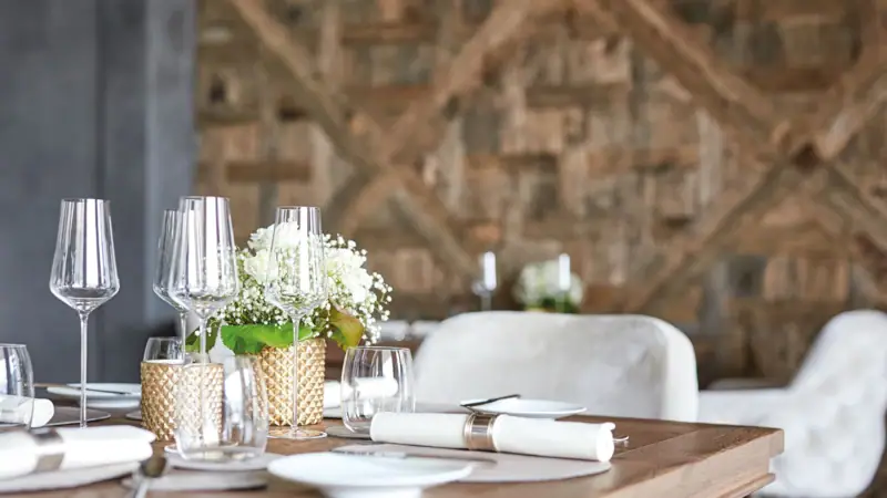 Sternerestaurant Kilian Stuba Ein Tisch mit Weingläsern und Blumenarrangement vor einer Holzvertäfelung..
