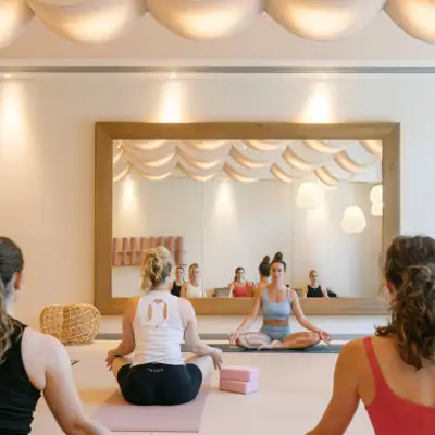 Yoga im A-ROSA Gardasee Eine Gruppe von Frauen sitzt in Yoga-Pose in einem Yoga-Raum mit einem Spiegel.