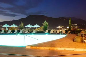 Gardasee Ein Swimmingpool mit Liegestühlen und Sonnenschirmen im Hintergrund.