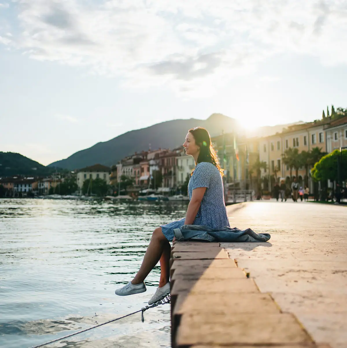 Strandpromenade von Salò Eine Frau sitzt auf einem Vorsprung am Wasser.