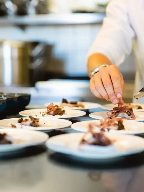 Tellerwerk Travemünde Eine Person richtet Essen auf Tellern an.
