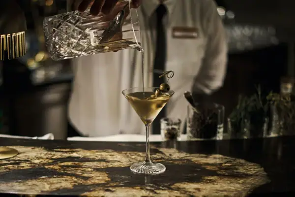 Eine Person gießt ein Getränk in ein Martiniglas ein.