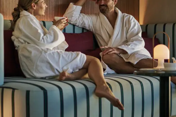 Wellness Ruhebereich Ein Mann und eine Frau in Bademänteln sitzen auf einem Sofa.