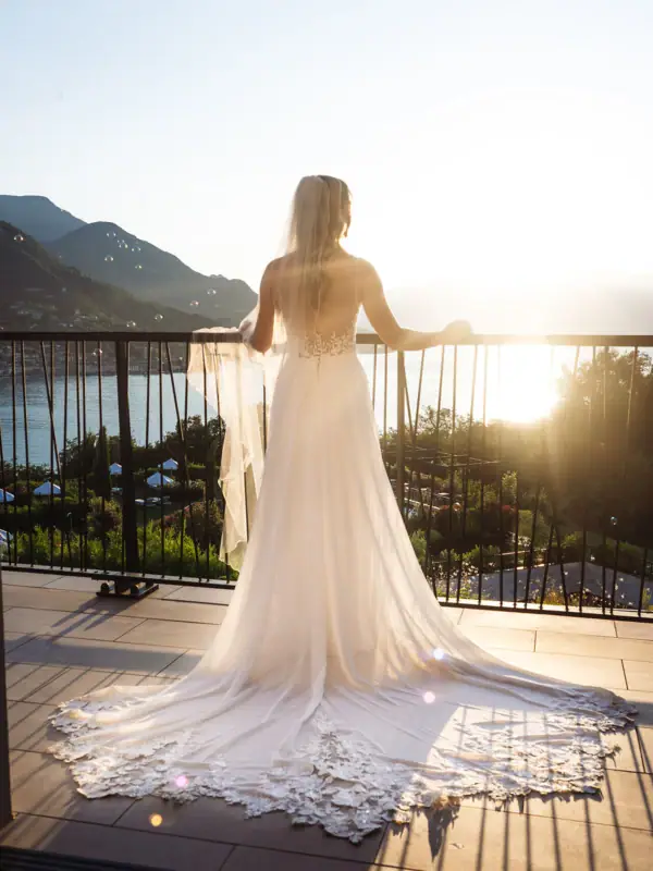 Braut auf der Terrasse mit Seeblick Eine Braut im weißen Kleid steht auf einer Terrasse und blickt auf den Gardasee im Abendlicht.