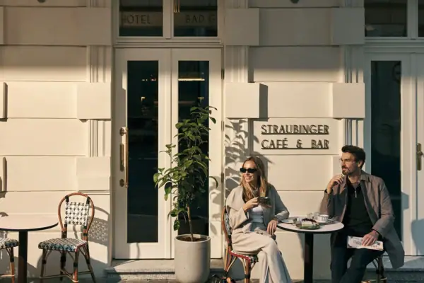 Kaffeehaus Gefühle am Straubingerplatz Ein paar sitzt an einem Tisch vor einem Café, isst Kuchen und schaut in die Ferne.