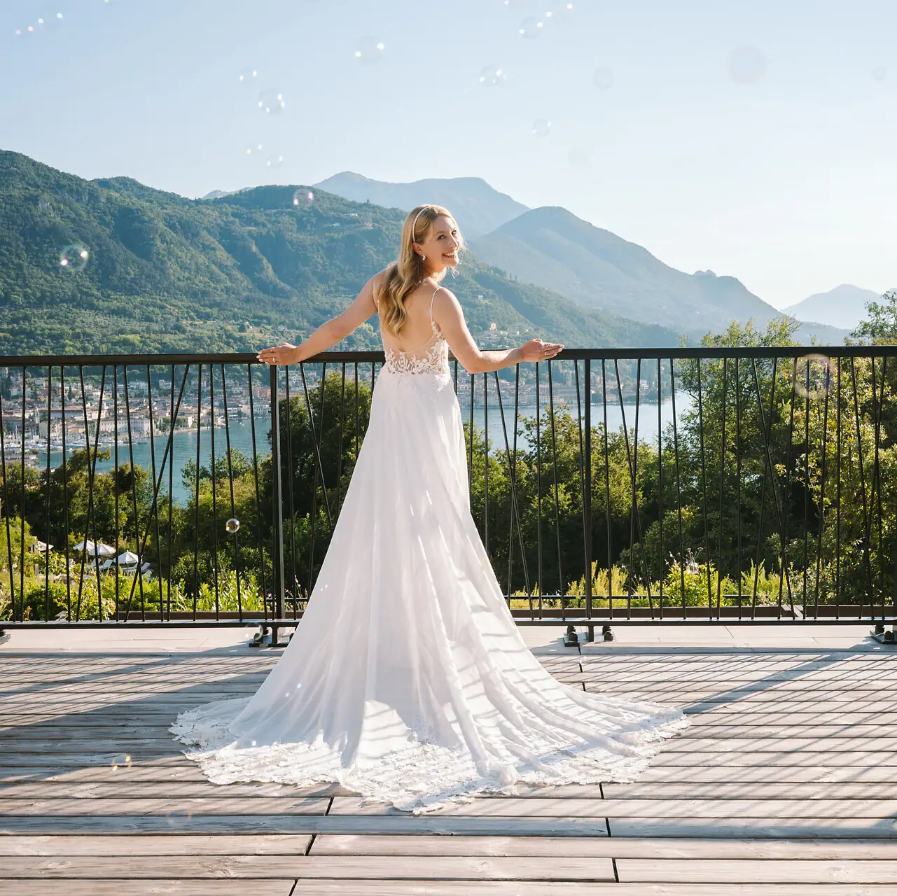 Heiraten am Gardasee Eine Frau in einem weißen Brautkleid steht auf einem Deck mit einem Geländer, im Hintergrund sind Berge zu sehen.